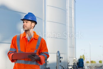 Male worker with clipboard below storage tanks