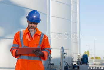 Male worker with clipboard below storage tanks