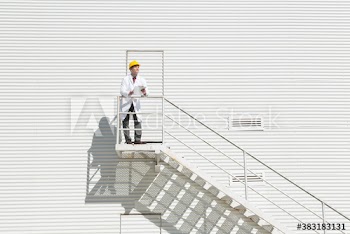 Male worker with clipboard in lab coat outside sunny dairy farm building