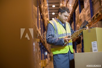 Male worker with clipboard scanning boxes in distribution warehouse
