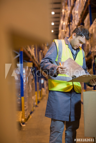 Male worker with clipboard working in distribution warehouse