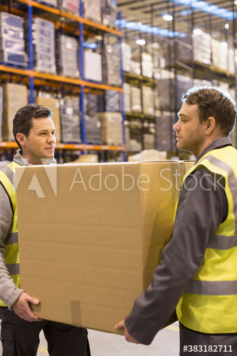 Male workers carrying box together in distribution warehouse