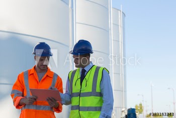 Male workers with clipboard talking below storage tanks