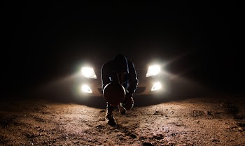 Man Against the Vehicle Headlight Squatting Holding Ball