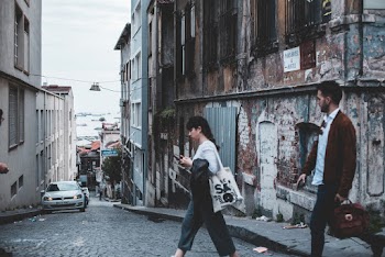Man and Woman Crossing A City Street With An Old Abandoned Building In The Corner