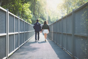 Man and Woman Holding Hand Walking on Grey Bridge