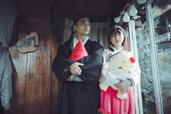 Man and Woman Holding Plush Toys Standing on Front of Brown Wall
