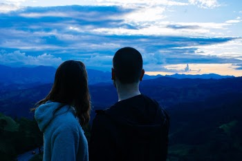 Man and Woman Overlooking Mountain Under Cloudy Sky