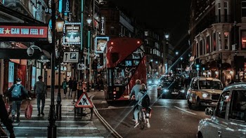 man and woman riding bicycle near city buildings with cars and bus during night time