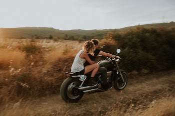 man and woman riding in motorcycle surrounded by brown and green field