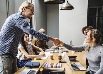 Man and Woman Shaking Hands in Middle of Brown Wooden Table