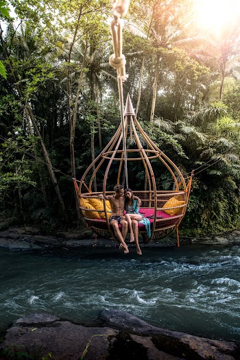 Man and Woman Sitting on Big Rattan Hammock Above River Surrounded With Green Trees
