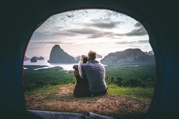 man and woman sitting on grass in front of mountains