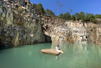Man and Woman Sitting on Mini Wooden Boat in the Middle of Body of Water Viewing Cliff and Trees Under Blue Skies