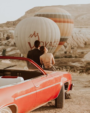 Man And Woman Sitting On Red Coupe Watching Hot Air Balloon
