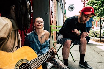 Man and Woman Sitting on Sidewalk and Playing Guitar