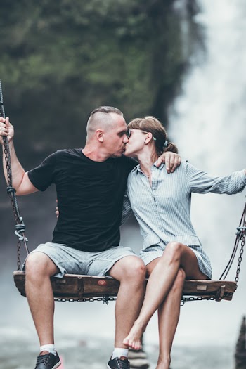 Man And Woman Sitting On Wooden Swing While Kissing