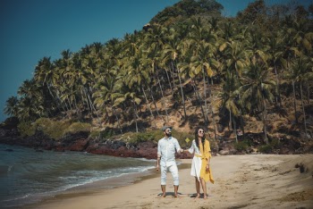 Man and Woman Standing on Seashore Near Mountain Covered With Coconut Trees