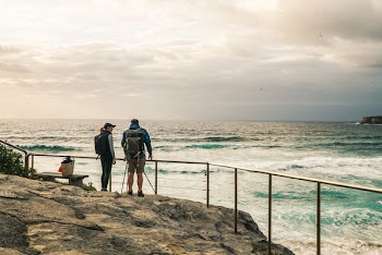 Man and Woman Standing on the Rocky Edge With Hand Rail Beside Ocean