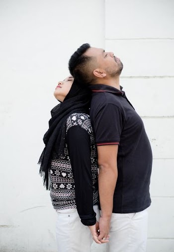 man and woman standing with their backs flat together near white wall