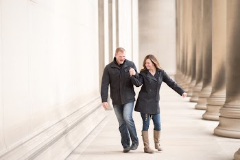 Man And Woman Wearing Black Coat And Jacket Walking Near Tall Pillars