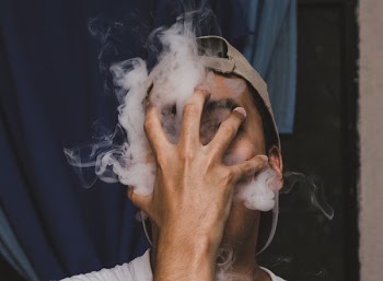man blowing smoke on his hand while wearing brown cap inside well lighted room