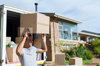 Man carrying cardboard box from moving van in sunny driveway