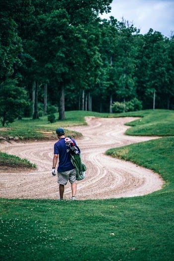man carrying golf bag along sand zone in golf course