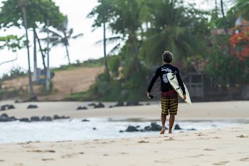 Man Carrying Surfboard While Walking On Seashore