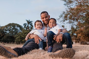 Man Carrying Two Boys While Sitting on Dried Grass Field