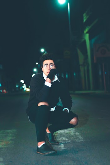Man Crouching on Road Outside Building at Night