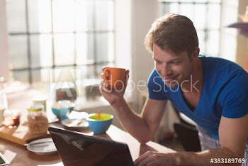 Man drinking coffee at laptop in morning kitchen