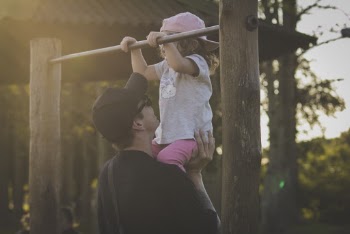 Man Helping Girl Exercise on Monkey Bar