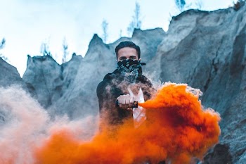 man holding a black vaporizer with orange smoke