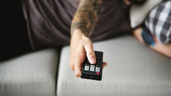 Man Holding Black Remote While Lying on Gray Sofa