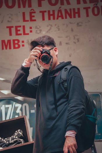 Man Holding Camera Beside Text Printed Wall