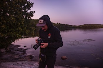 Man Holding Camera While Standing Near Body Of Water