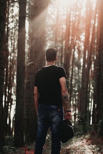 man holding cap standing in forest