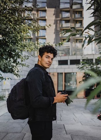 man holding DSLR camera carrying backpack near building