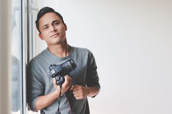 man holding DSLR camera leaning on windowpane