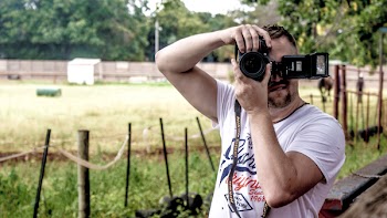 Man Holding Dslr Camera While Standing Near Fence