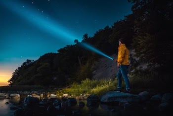 man holding flashlight standing on gray stone during nighttime