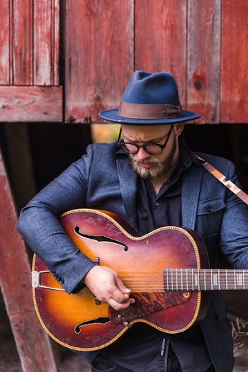 Man Holding Jazz Guitar Standing Beside Brown Wooden Wall