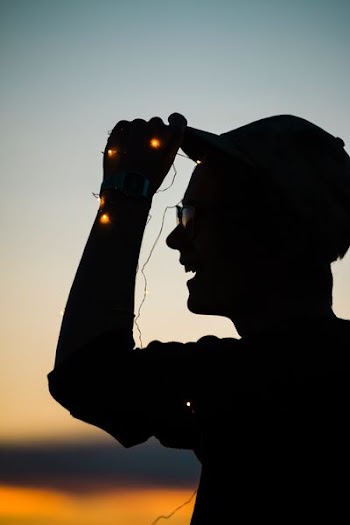 man holding on hat while laughing silhouette