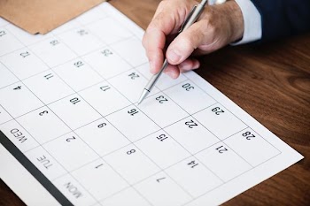 man holding pen pointing on calendar