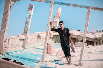 Man Holding Shoes While Leaning on Wooden Pole