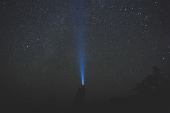 man holding turned on flashlight outdoor during nighttime
