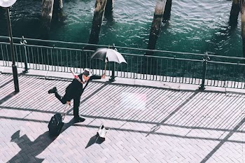 man holding umbrella and trolley bag on bridge