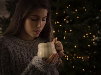 man holding white ceramic mug standing in front of lighted green Christmas tree