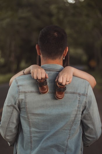 Man Hugging Woman Holding Baby Shoes